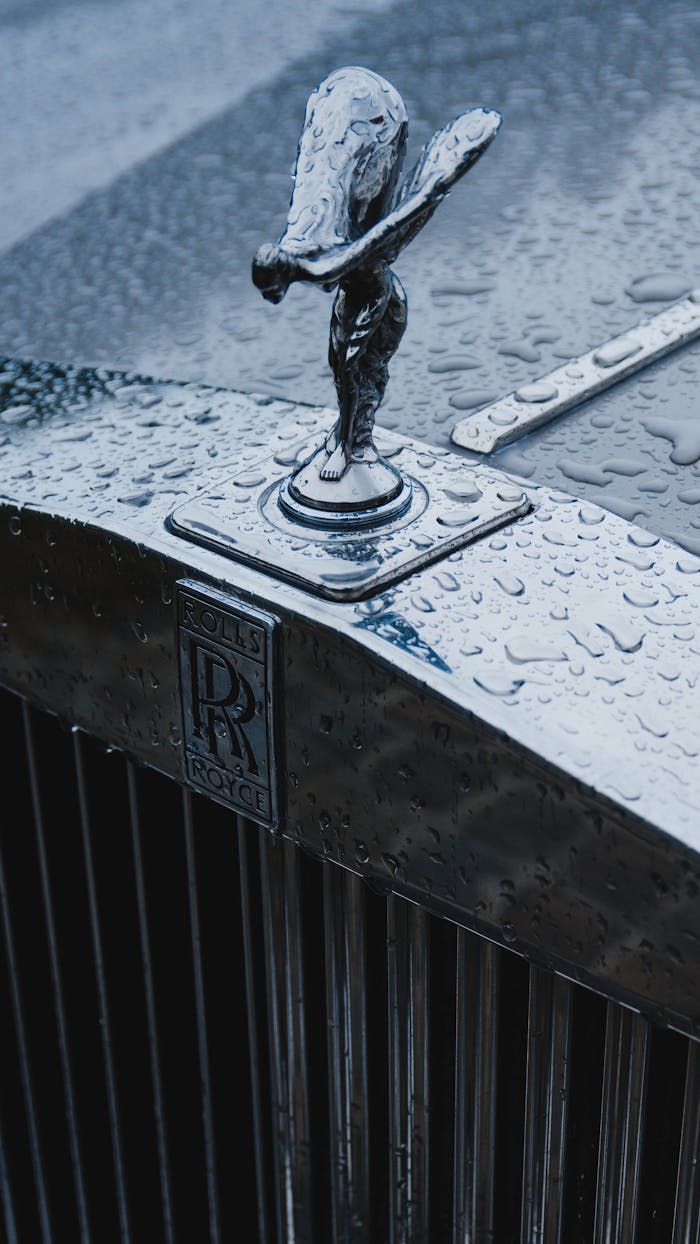 Close-up of a Rolls-Royce hood ornament with raindrops, showcasing luxury and detail.