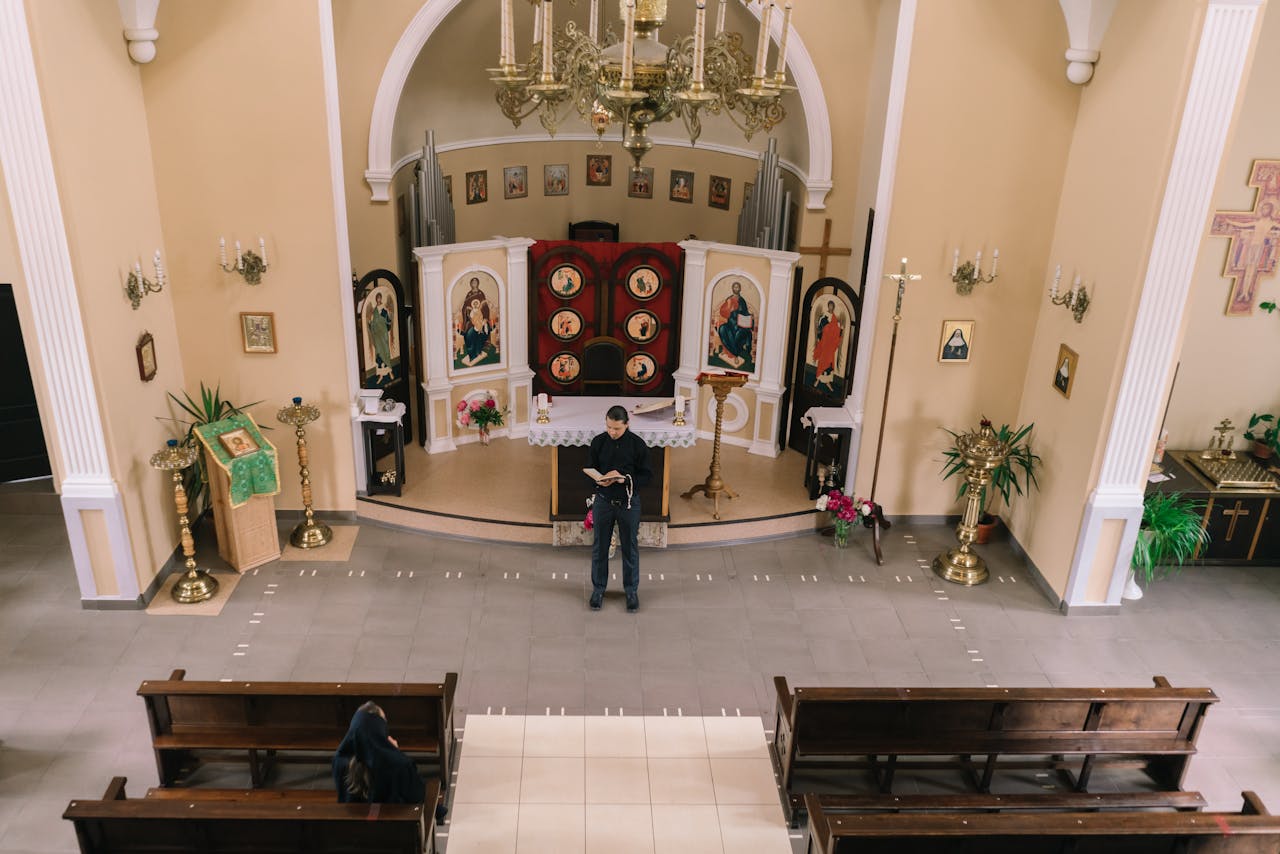 Priest reading from a book inside a church with icons and pews visible.